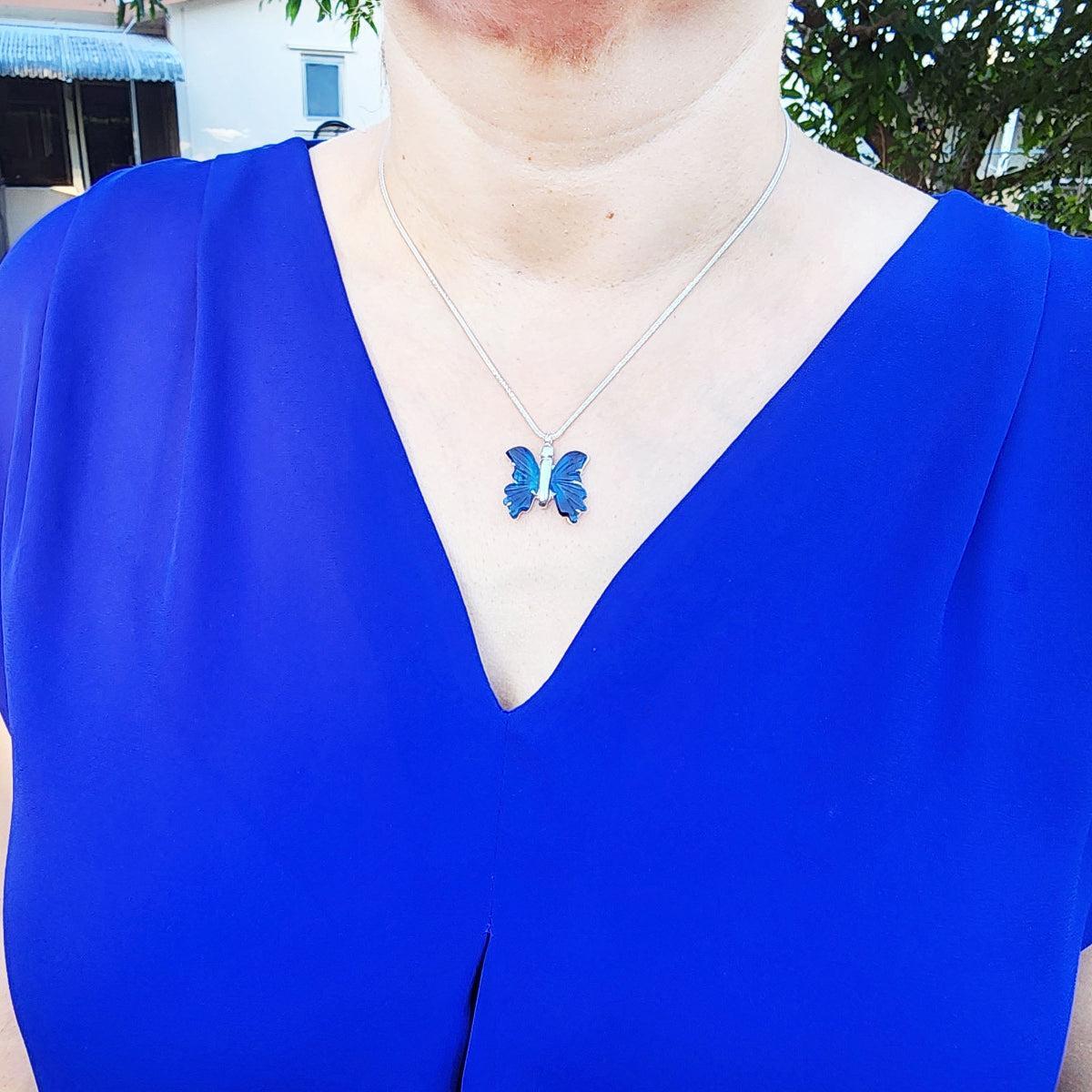 Person wearing a blue dress with a butterfly agate necklace