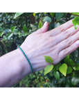Hand wearing a natural round cut emerald tennis bracelet with a leafy background.
