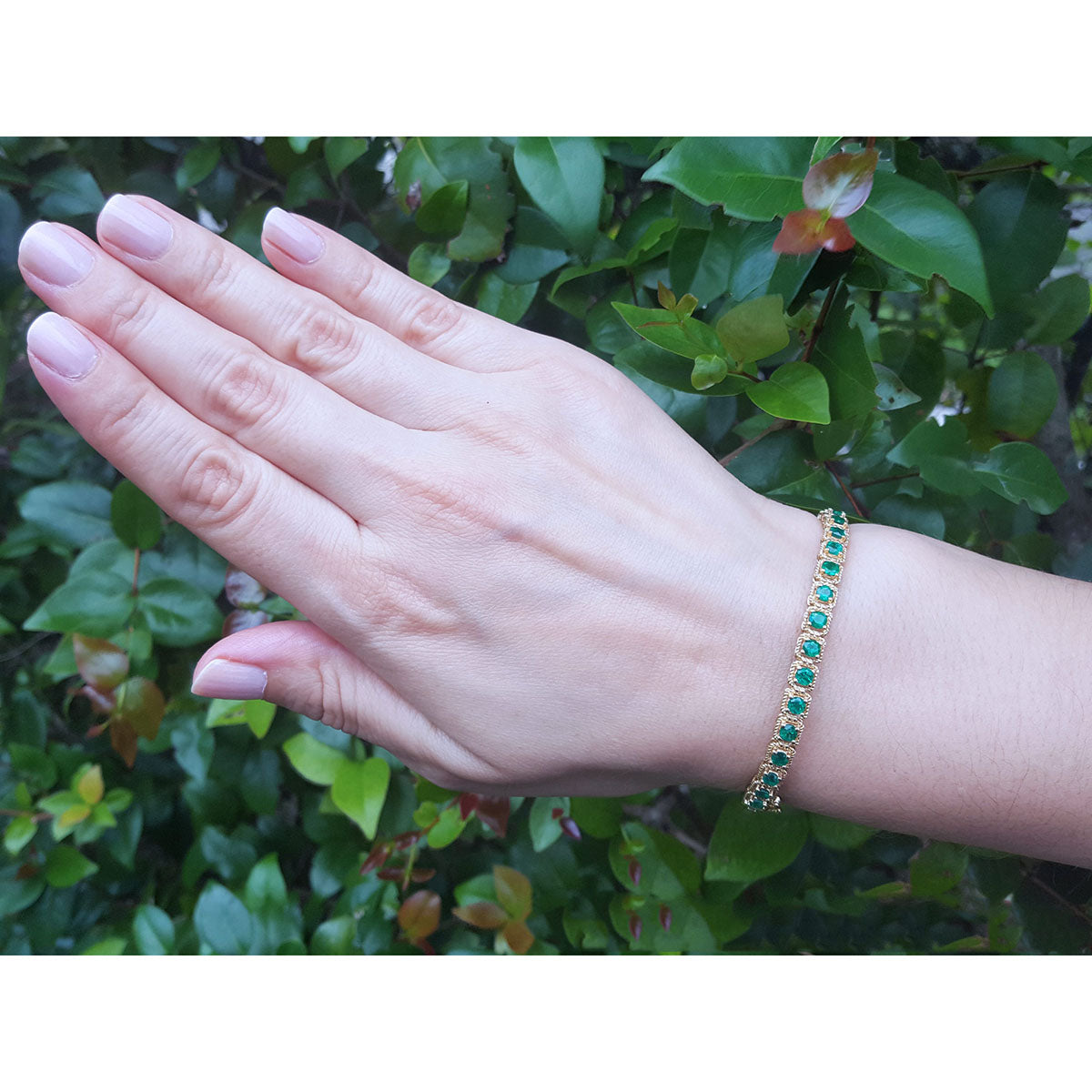 A woman&#39;s hand wearing a emerald bangle bracelet with a leafy background.