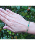 A woman's hand wearing a emerald bangle bracelet with a leafy background.