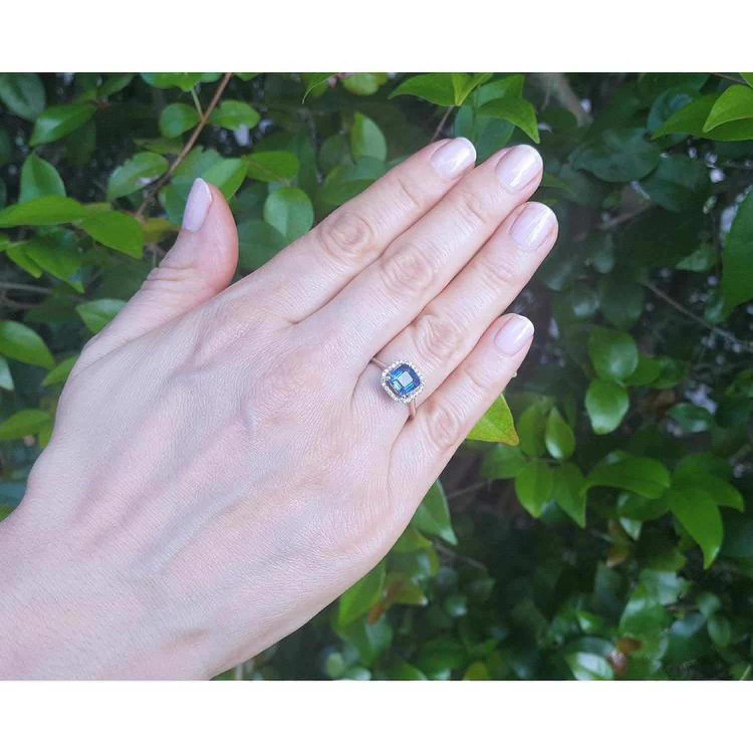Asscher cut blue sapphire ring with halo diamonds in 18k white gold on a hand.