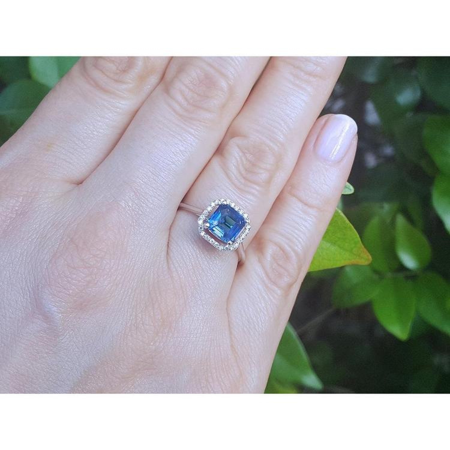 Asscher cut blue sapphire ring with halo diamonds on an 18k white gold band, worn on a hand.