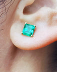 Close-up of an ascher cut emerald stud earring on an ear.