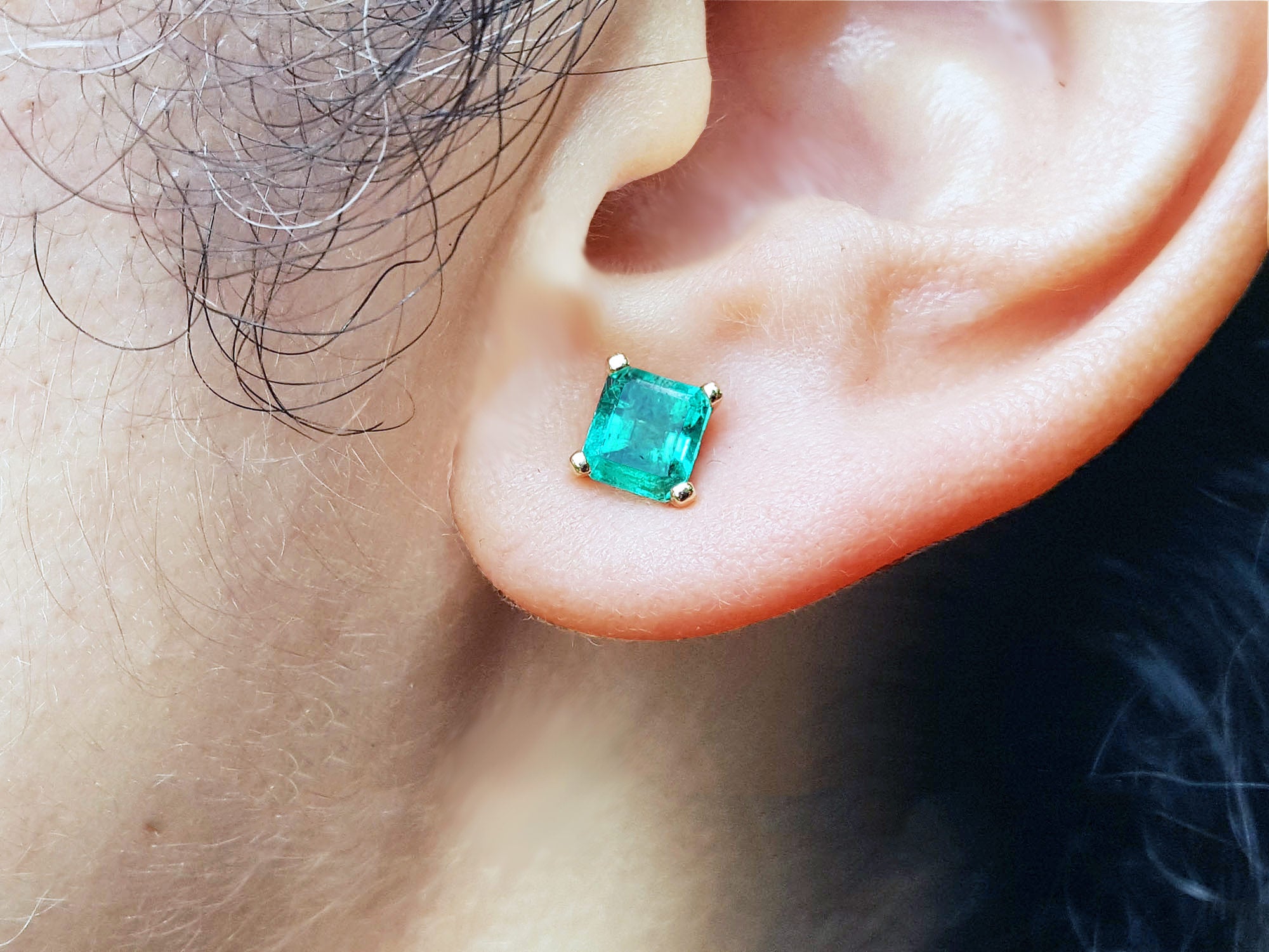 Close-up of an ear wearing an Asscher cut emerald stud earring.
