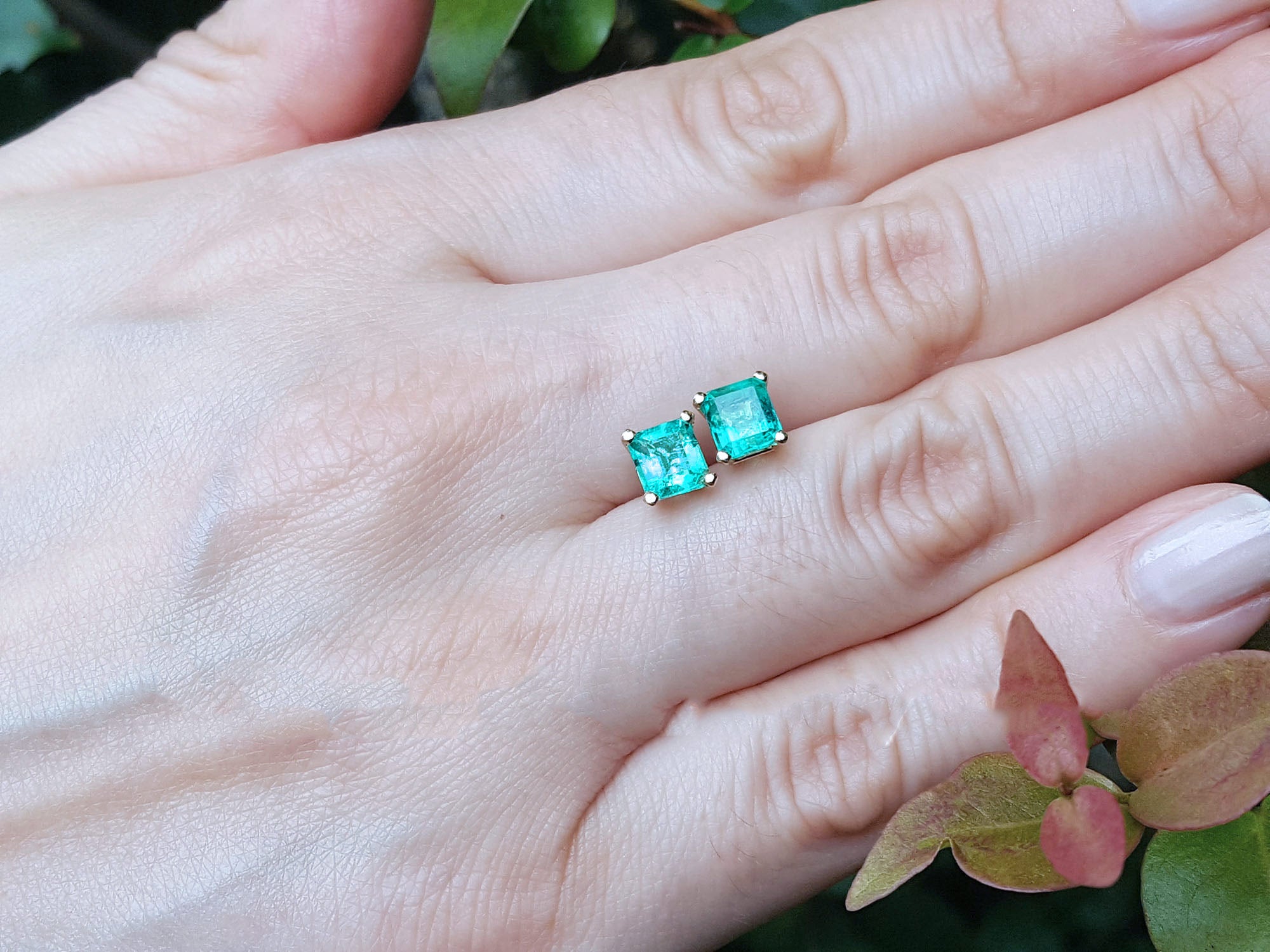  Asscher cut emerald stud earrings on a hand with a natural background.