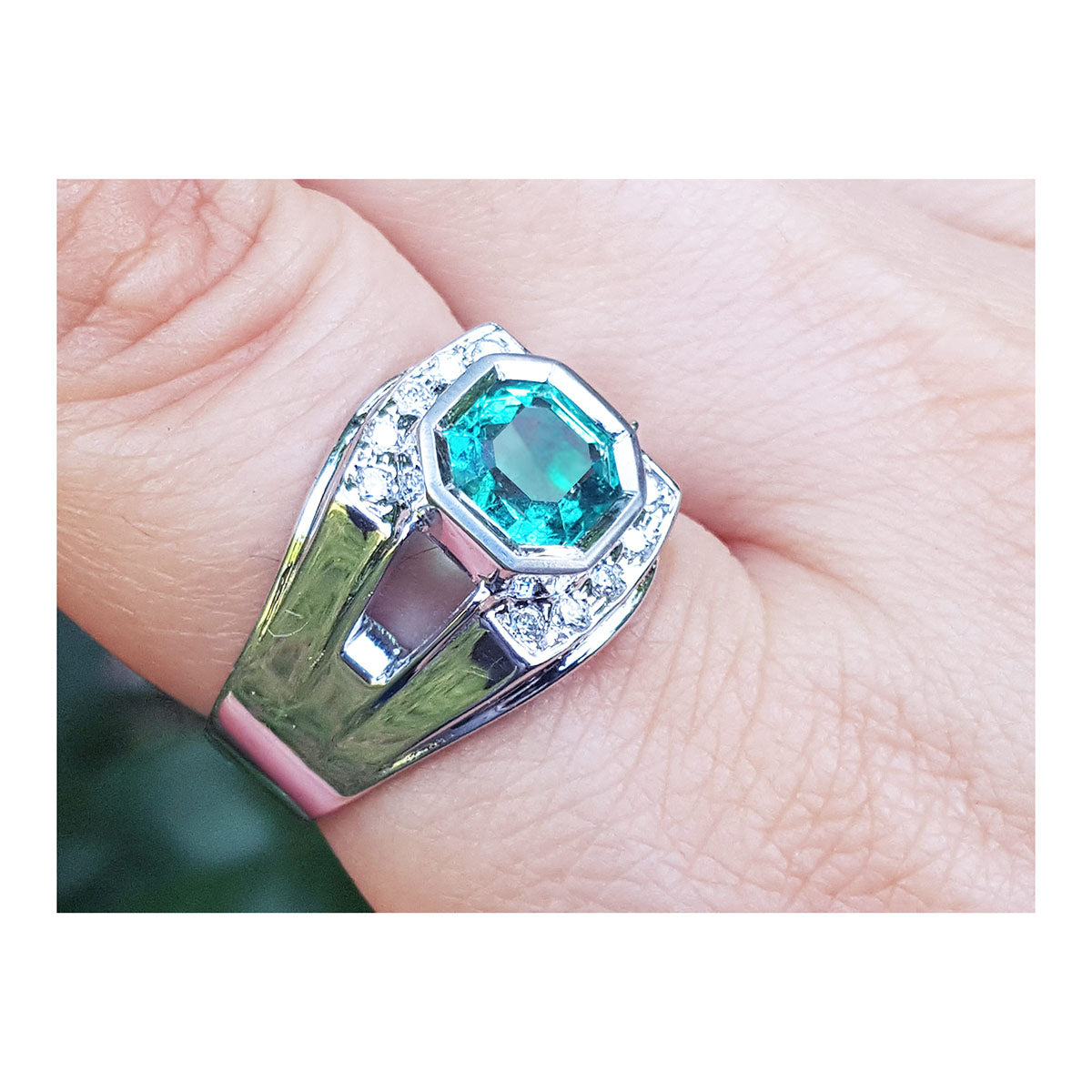 A men's asscher cut emerald ring in white gold on a finger.