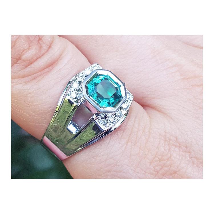 A men's asscher cut emerald ring in white gold on a finger.