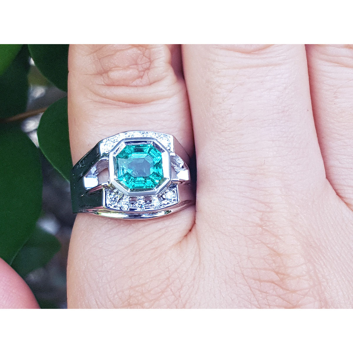 A men&#39;s emerald ring white gold on a finger against a natural background.