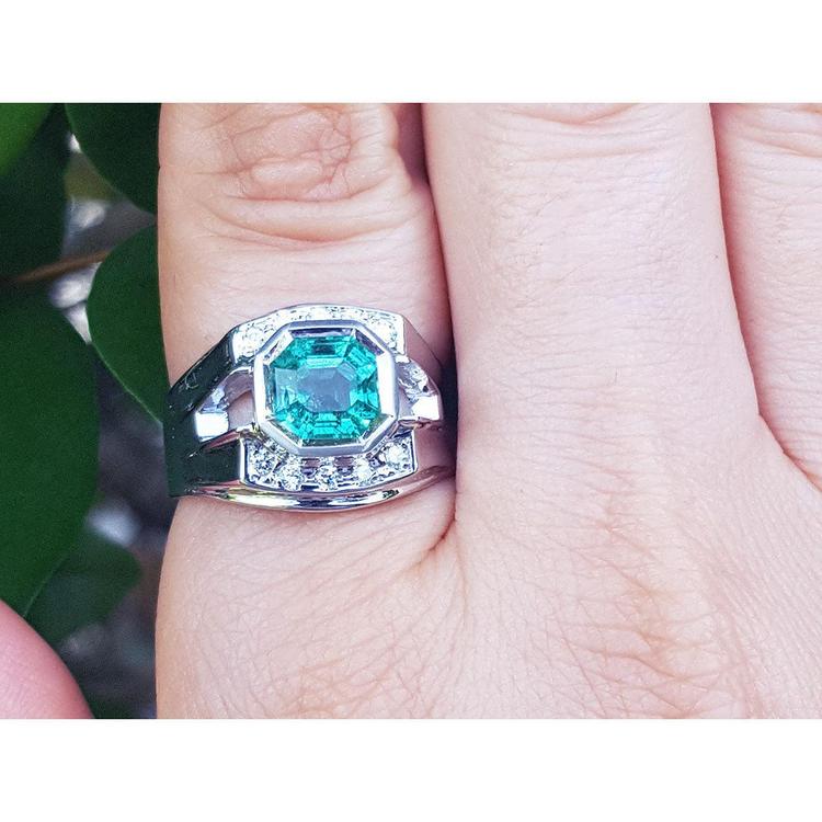 A men's emerald ring white gold on a finger against a natural background.