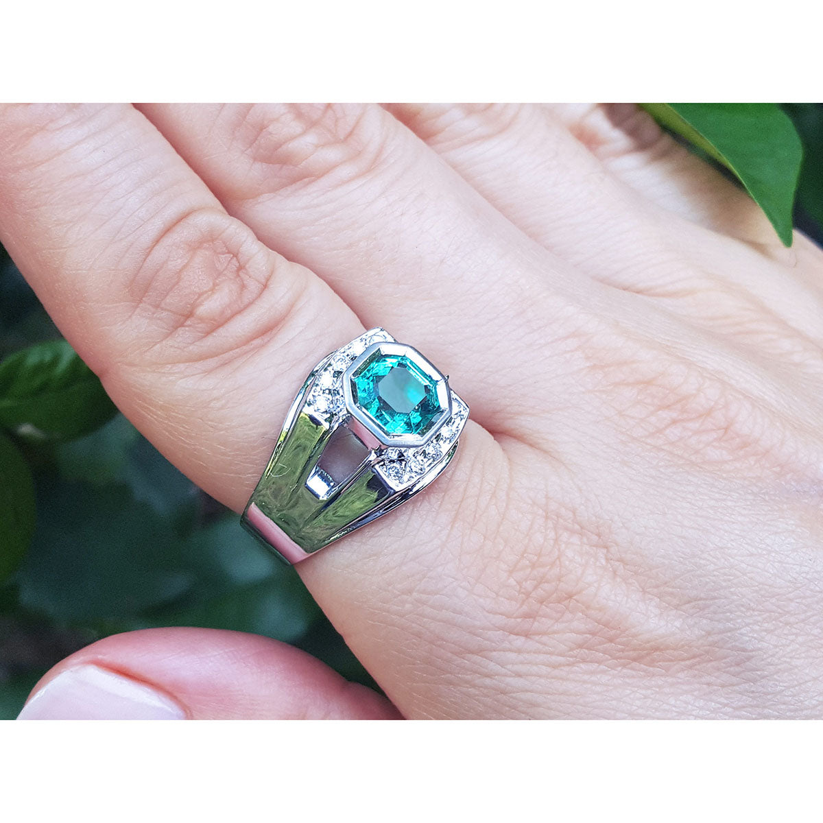 A men&#39;s emerald ring in white gold on a hand against a natural background.