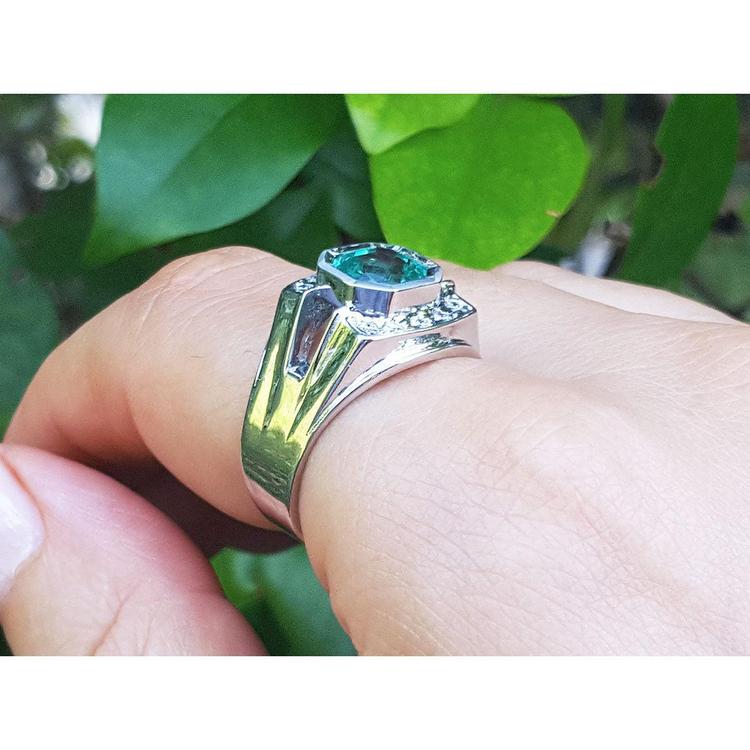 A men's emerald ring underside view on a finger against a green leafy background.