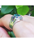 A men's emerald ring underside view on a finger against a green leafy background.