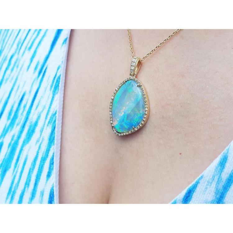 Opal pendant necklace on a person wearing a blue and white patterned top.