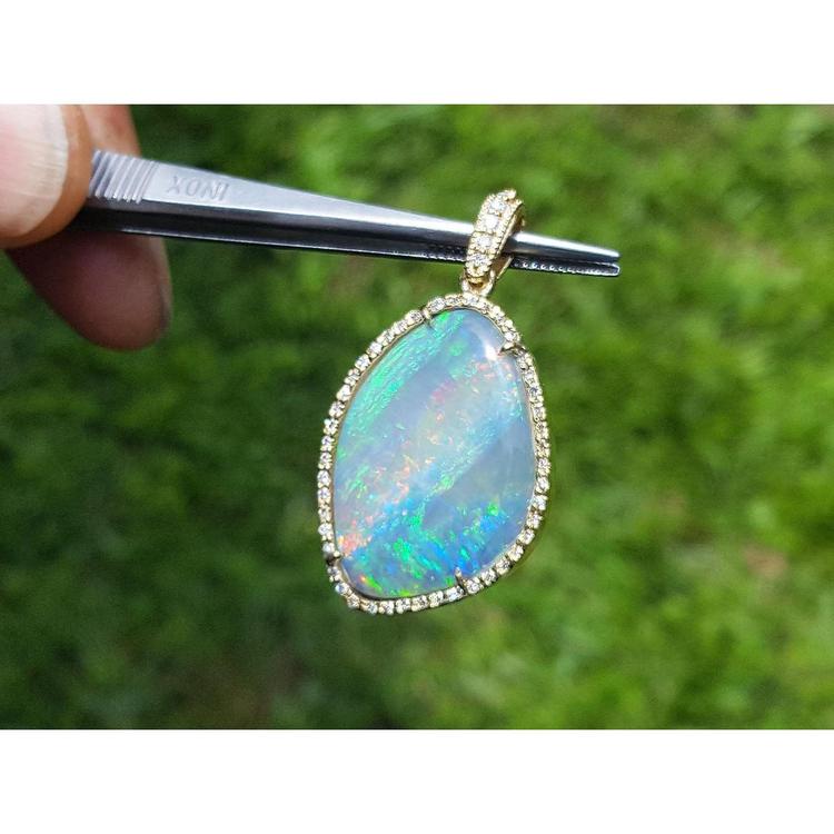 Opal pendant held by tweezers with a blurred green background.