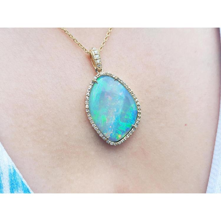 Opal pendant necklace on a person's neck with a pink skin background.