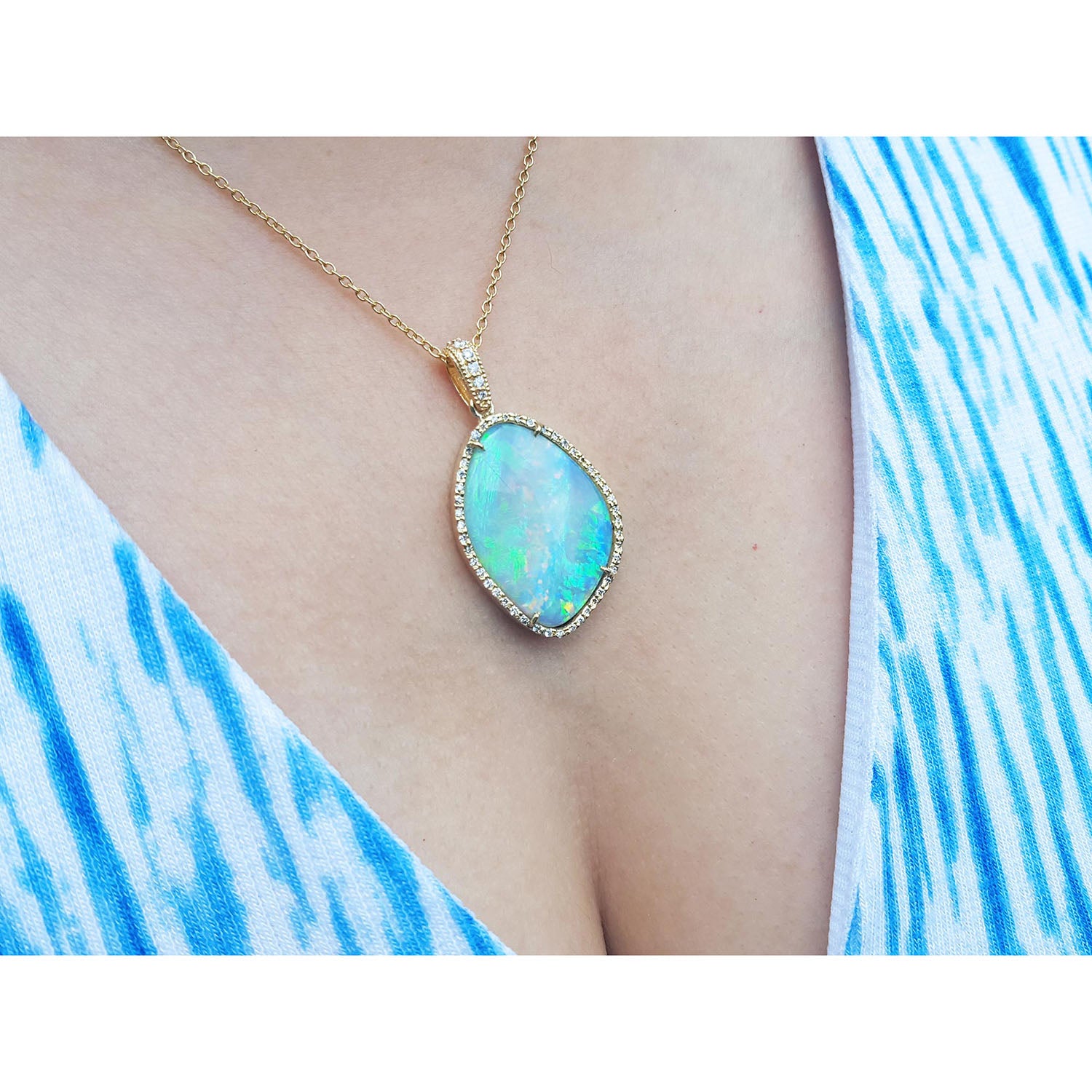 Opal necklace with gold chain on a person wearing a blue and white patterned top.