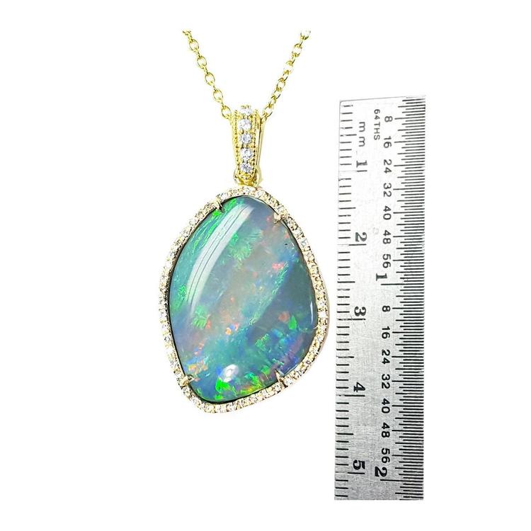 Opal pendant necklace with gold chain next to a ruler for size reference on a white background