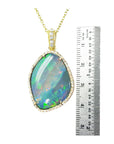 Opal pendant necklace with gold chain next to a ruler for size reference on a white background
