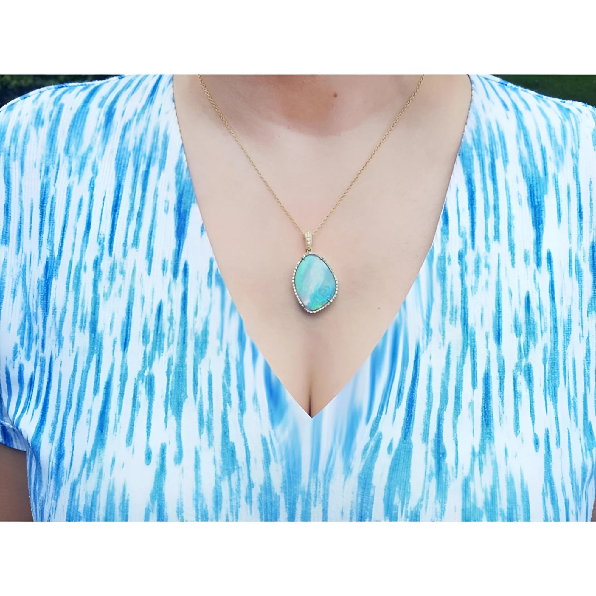 Australian opal pendant with bluish-green play-of-color, handcrafted in 18K yellow gold, worn on a woman.