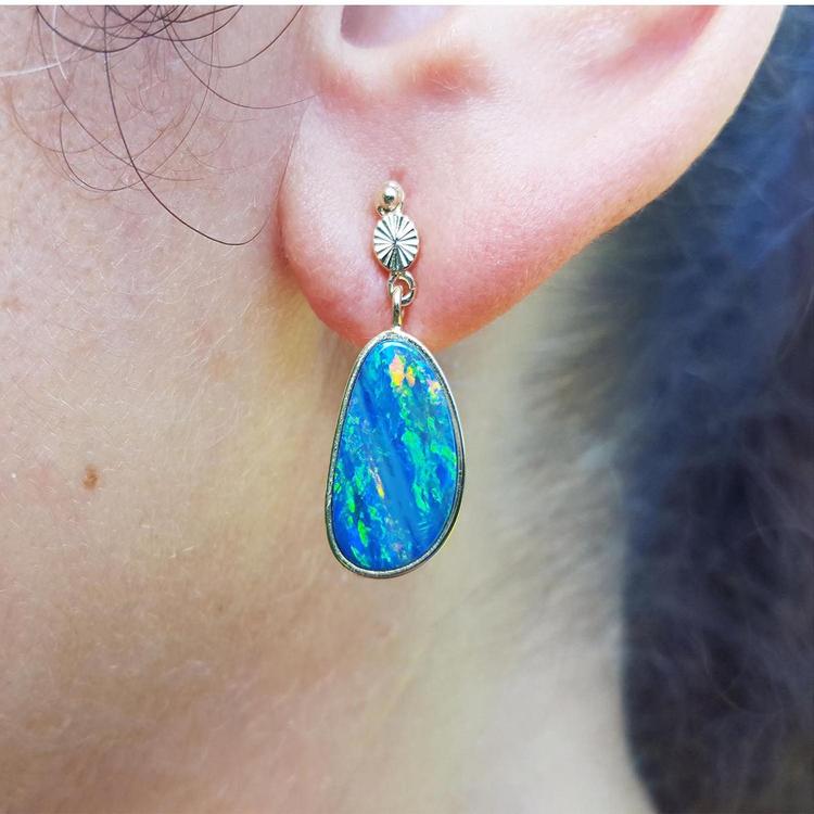 Close-up of an ear wearing a blue opal earring with a 14k yellow gold setting.