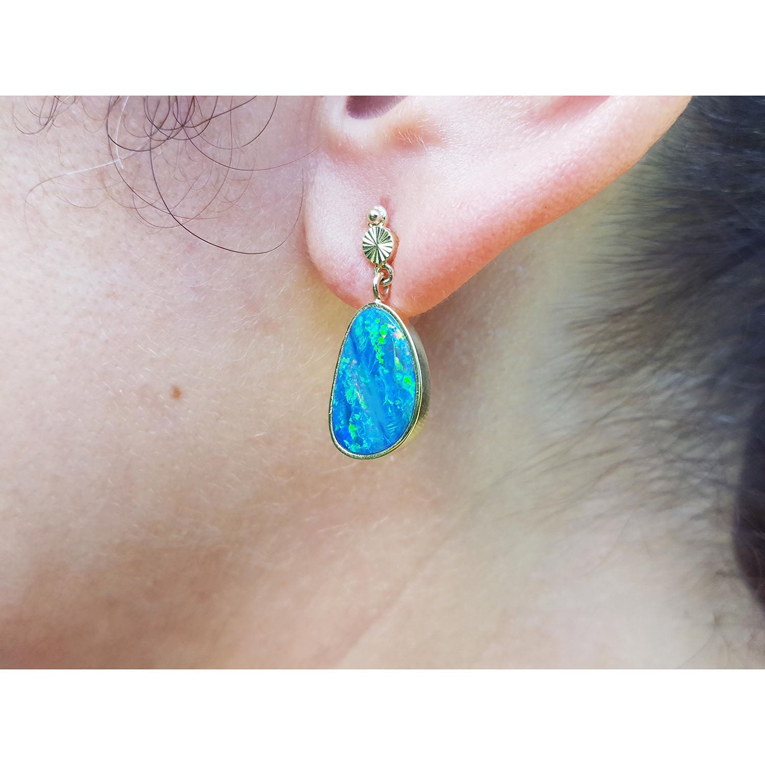 Close-up of an ear wearing a blue opal earring with yellow gold setting.