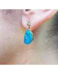 Close-up of an ear wearing a blue opal earring with yellow gold setting.