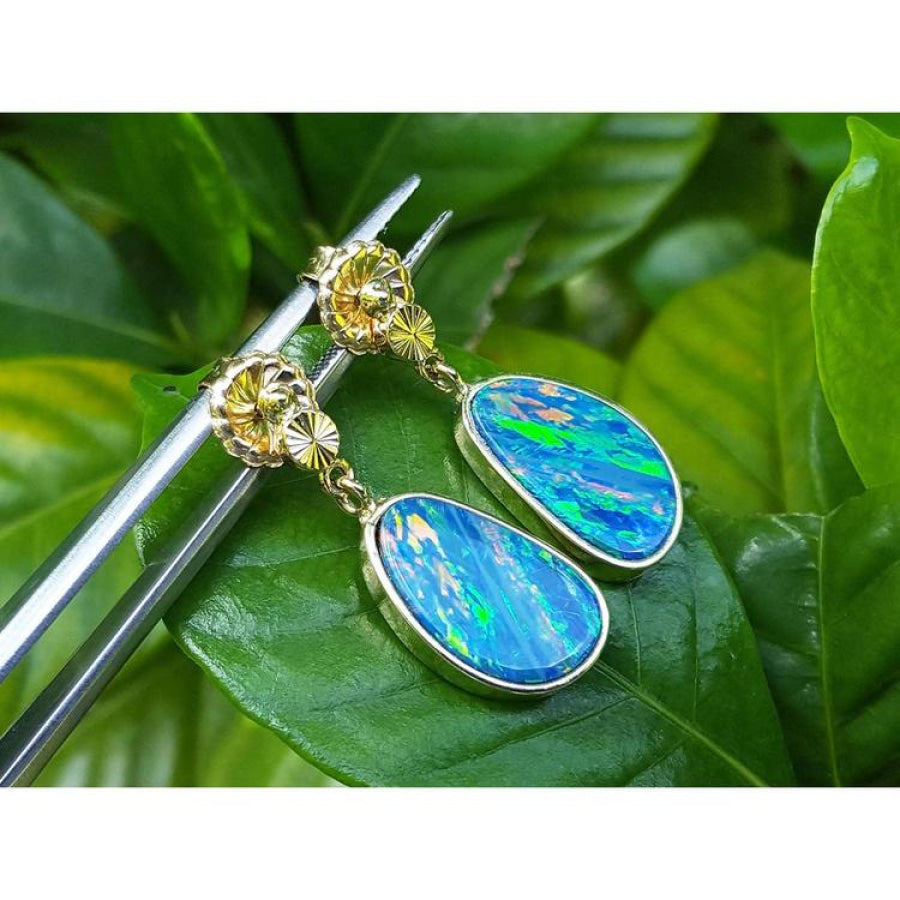 14K yellow gold dangle earrings with oval Australian opal doublets, bezel set, on a green leaf.