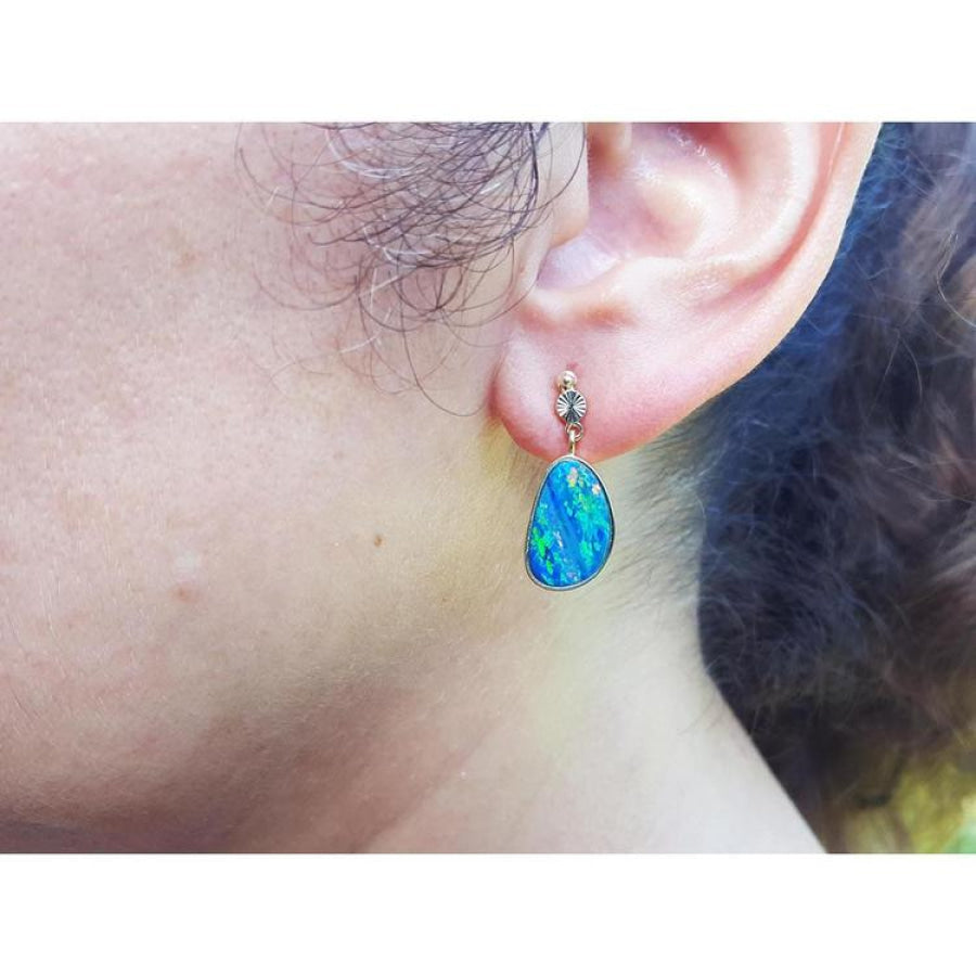 Australian opal doublet dangle earring in 14K yellow gold with bezel setting, worn on an ear.