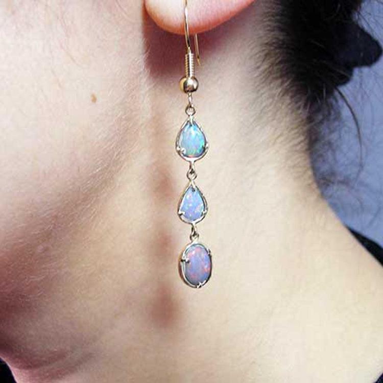 Close-up of a woman wearing a set of opal teardrop earrings.= in yellow gold.