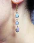 Close-up of a woman wearing a set of opal teardrop earrings.= in yellow gold.