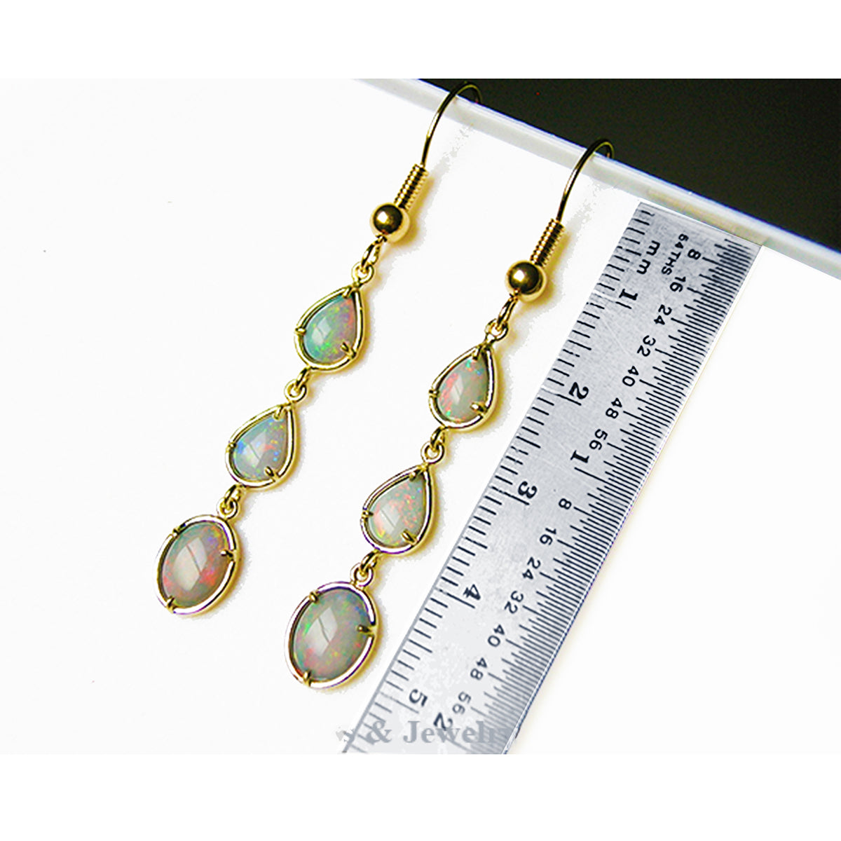 Gold earrings with natural Australian opal stones next to a ruler for size reference on a white background.