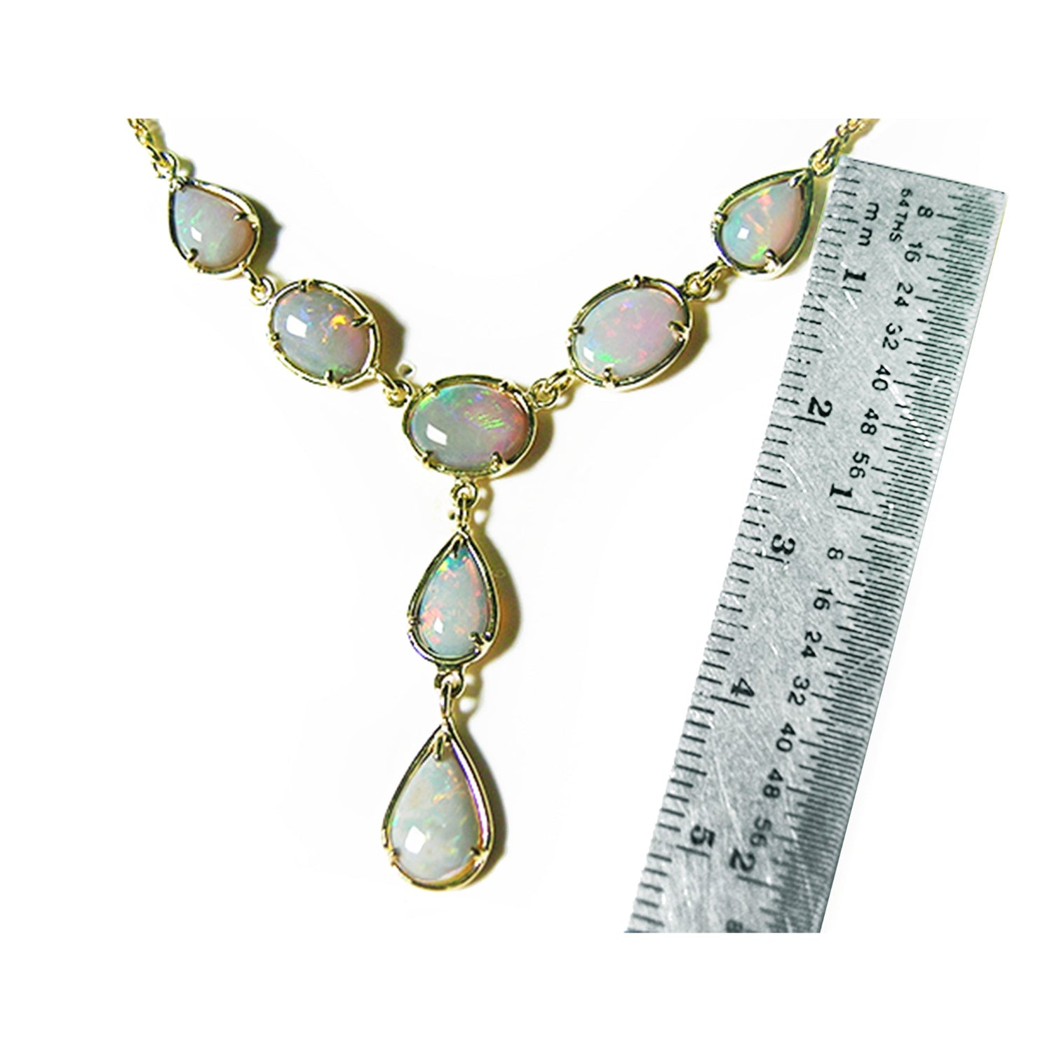 A natural opal necklace with gold setting next to a ruler on a white background.