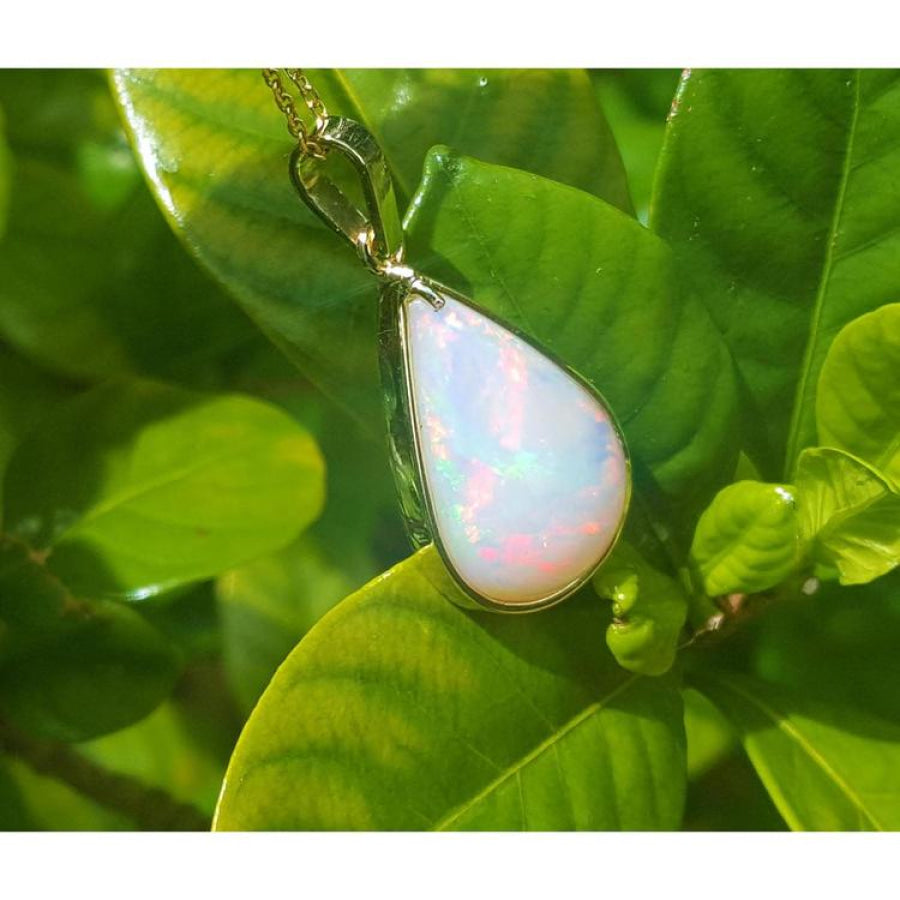 Pear-shaped Australian opal pendant with red-orange flashes in 14k yellow gold, on green leaves.