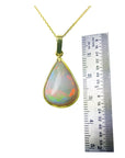 Opal pendant on a gold chain with a ruler for scale on a white background