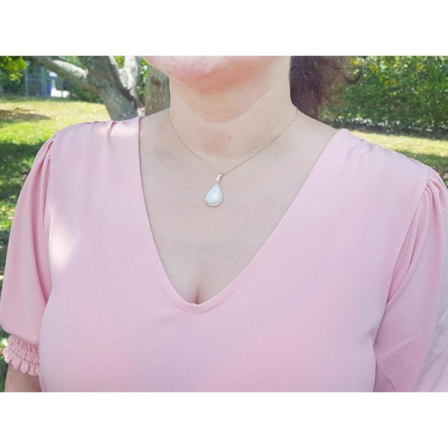 Pear-shaped Australian opal pendant with red-orange flashes on a 14k yellow gold chain, worn on a woman.