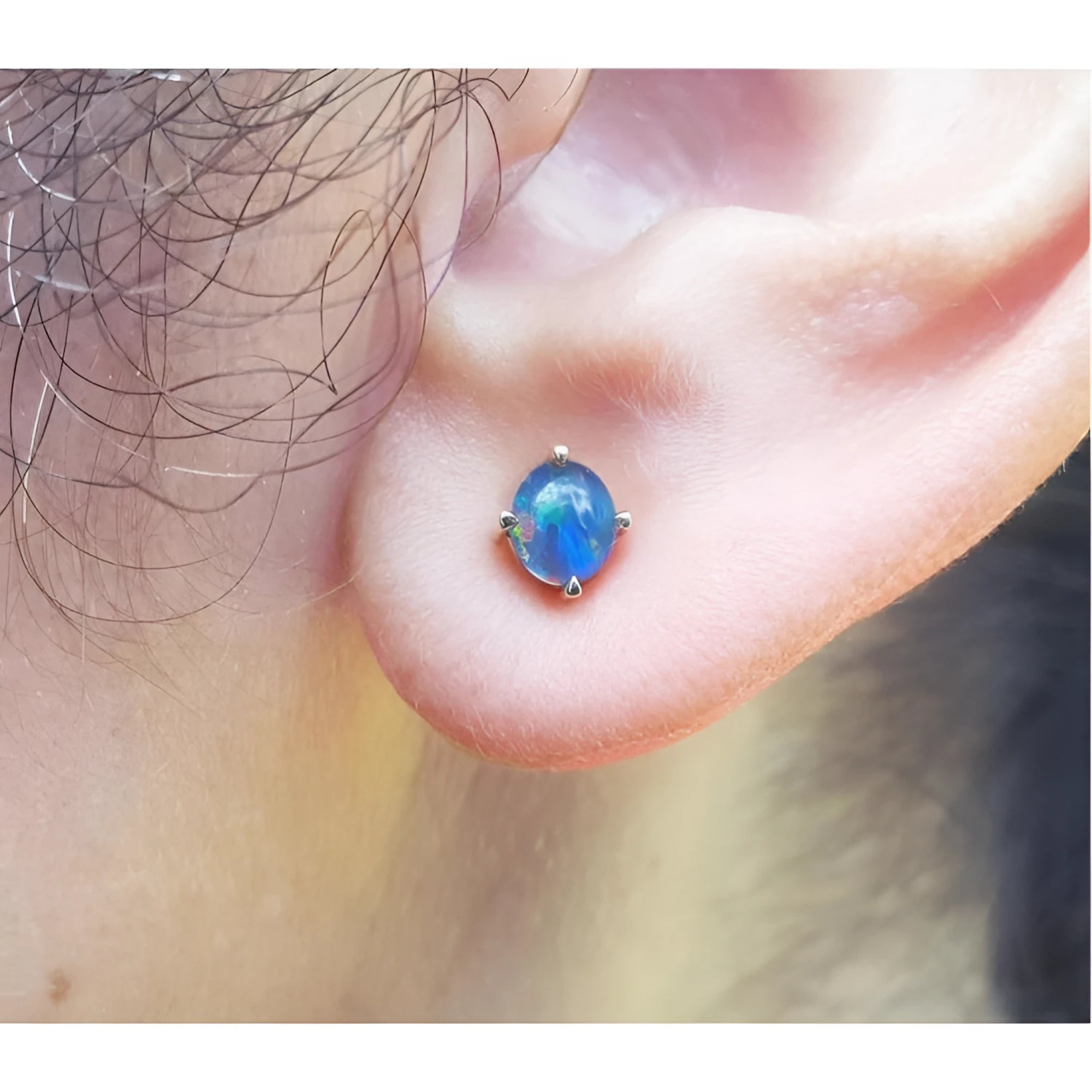 Round Australian opal doublet stud earring with blue and green colors, prong-set in 14K yellow gold on an earlobe.