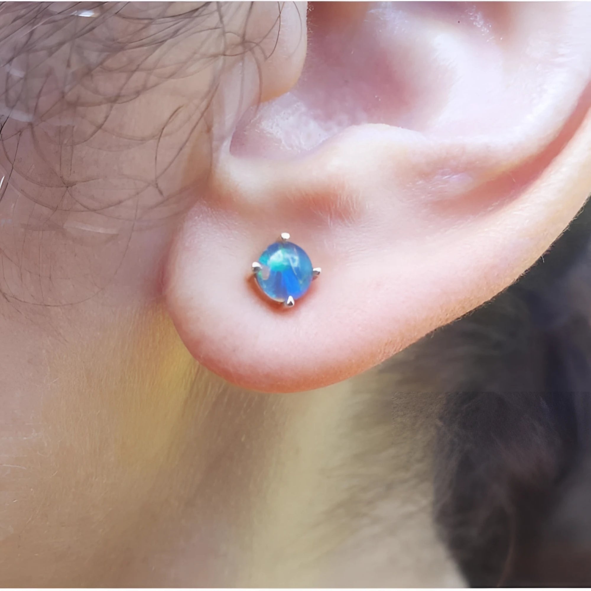 Round Australian opal doublet stud earring with blue play-of-color, prong-set in 14K gold on an earlobe.