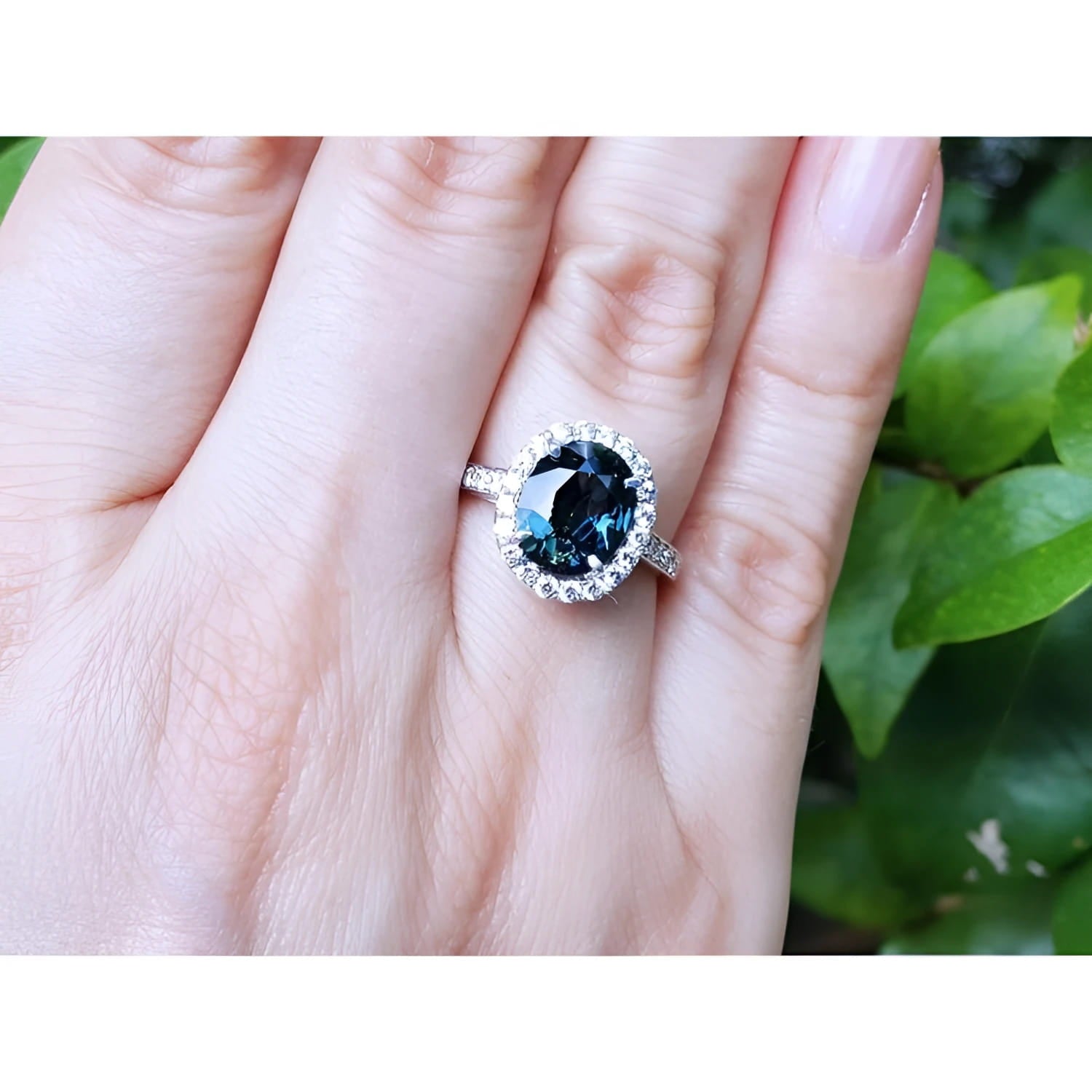 2.82 carat oval bluish-green Australian sapphire ring with diamond halo in 18K white gold on a hand.