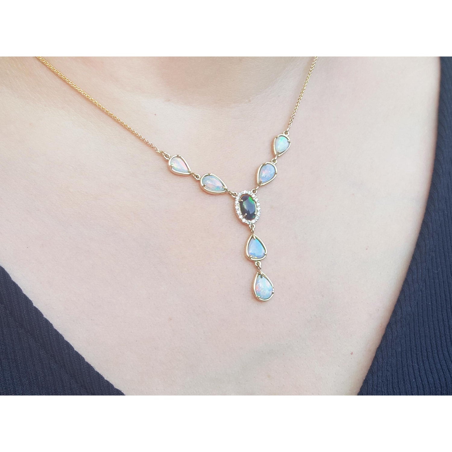 Necklace with a pendant featuring opal stones on a person wearing a dark blue top.