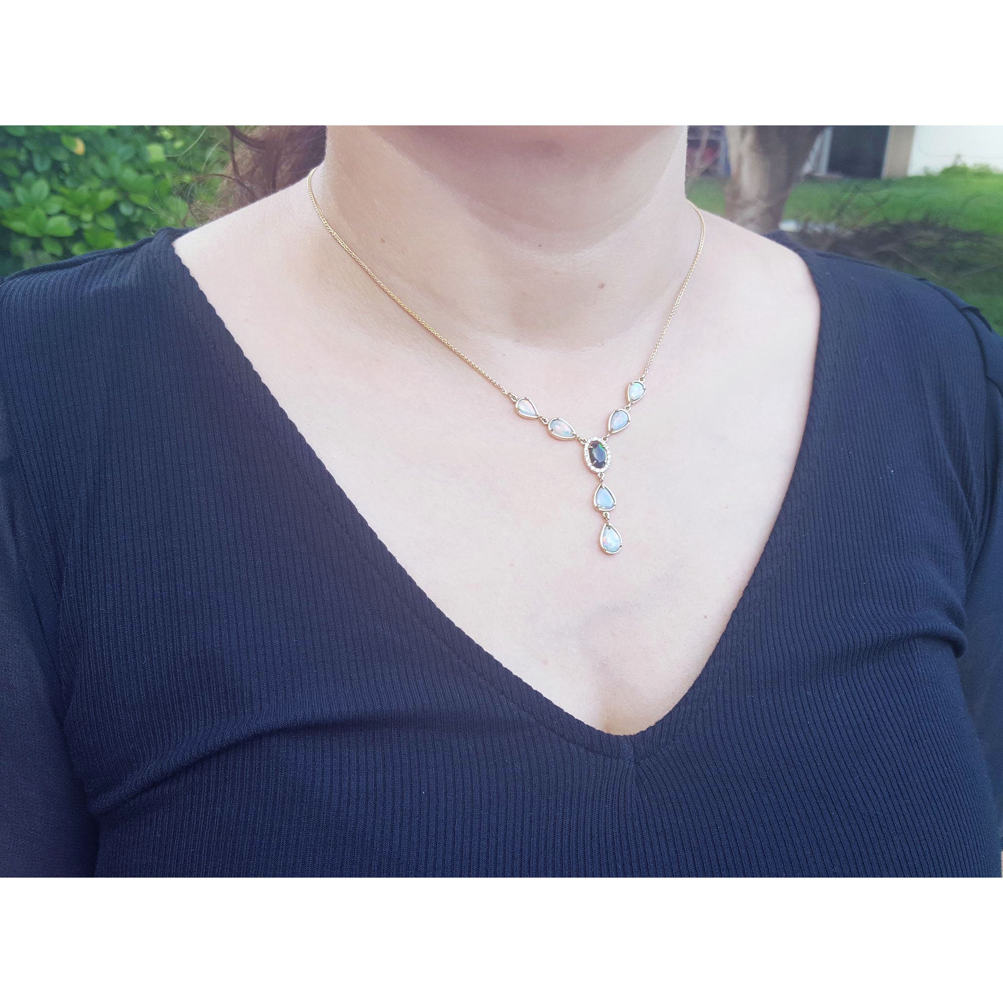 Person wearing a necklace with a blue gemstone pendant against a blurred outdoor background