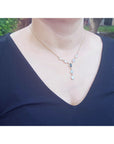Person wearing a necklace with a blue gemstone pendant against a blurred outdoor background