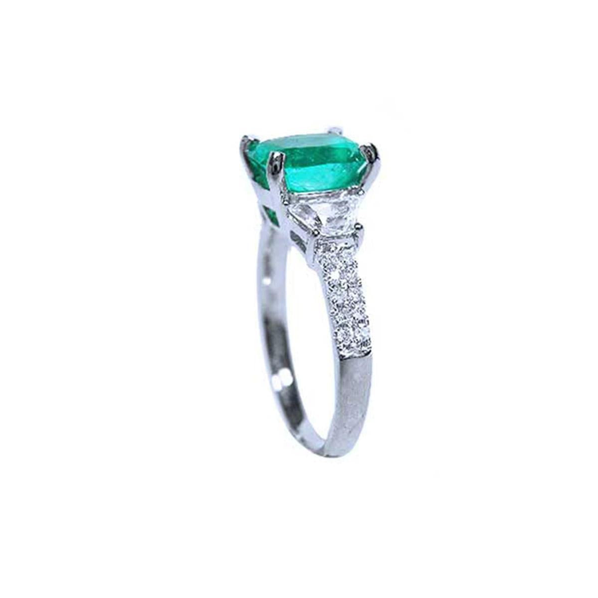 Half side profile of a cushion cut emerald ring, from the top, trapezoid diamond shoulders and accent diamonds on the shank visibles.