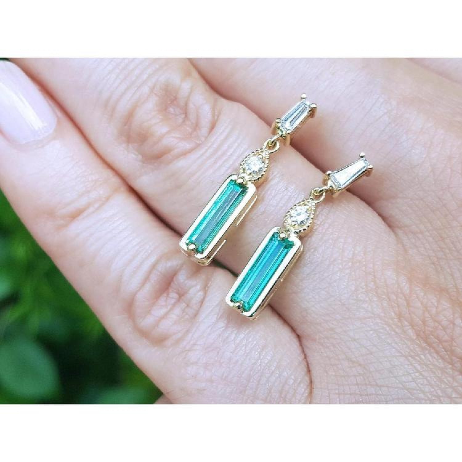 14K gold stud earrings with baguette-cut Colombian emeralds, pear-shaped extensions, and tapered baguette diamonds.