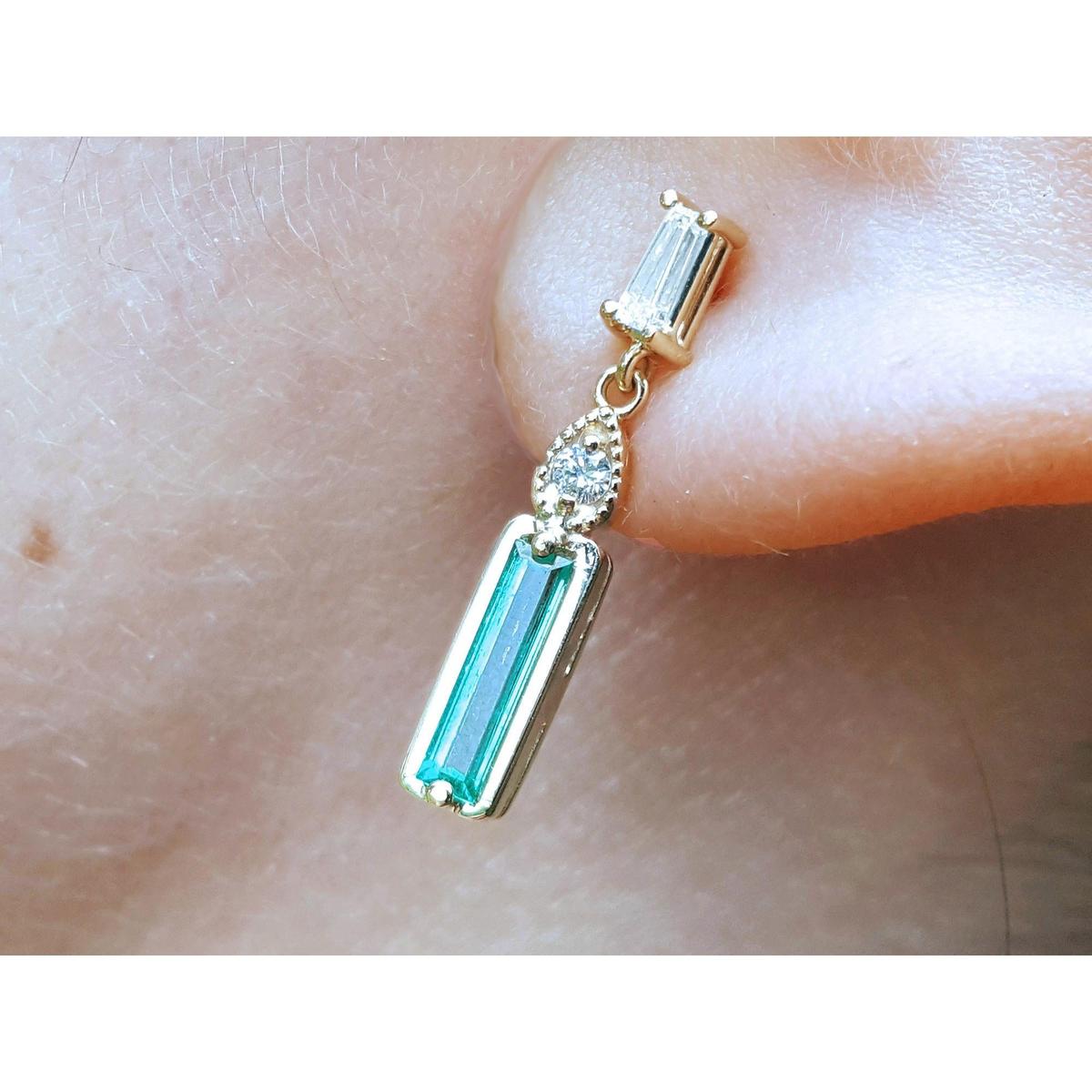 Dangle baguette cut emerald stud earrings on a person's ear