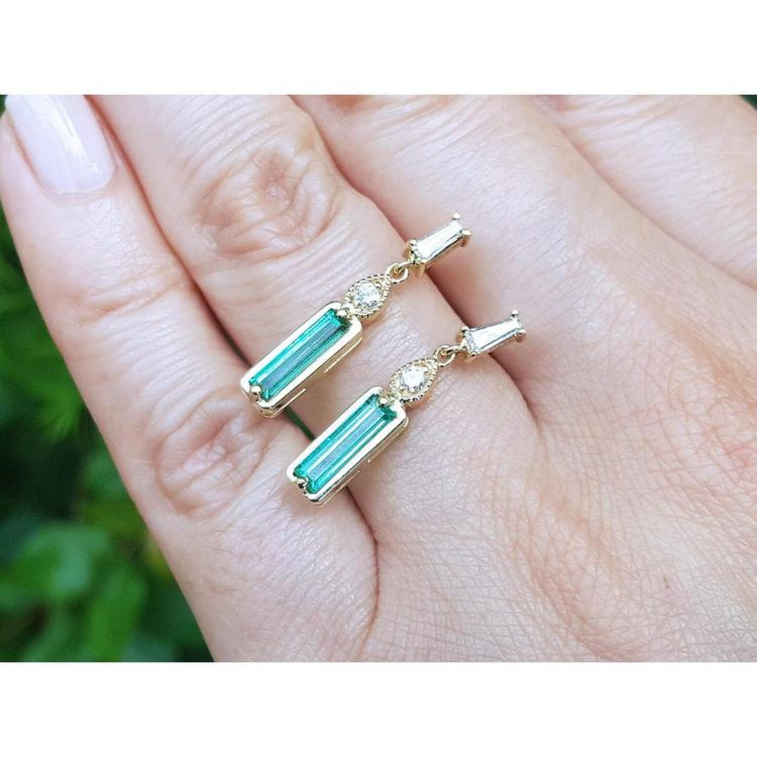14K gold stud earrings with baguette-cut emeralds, pear-shaped extensions, and tapered baguette diamonds.
