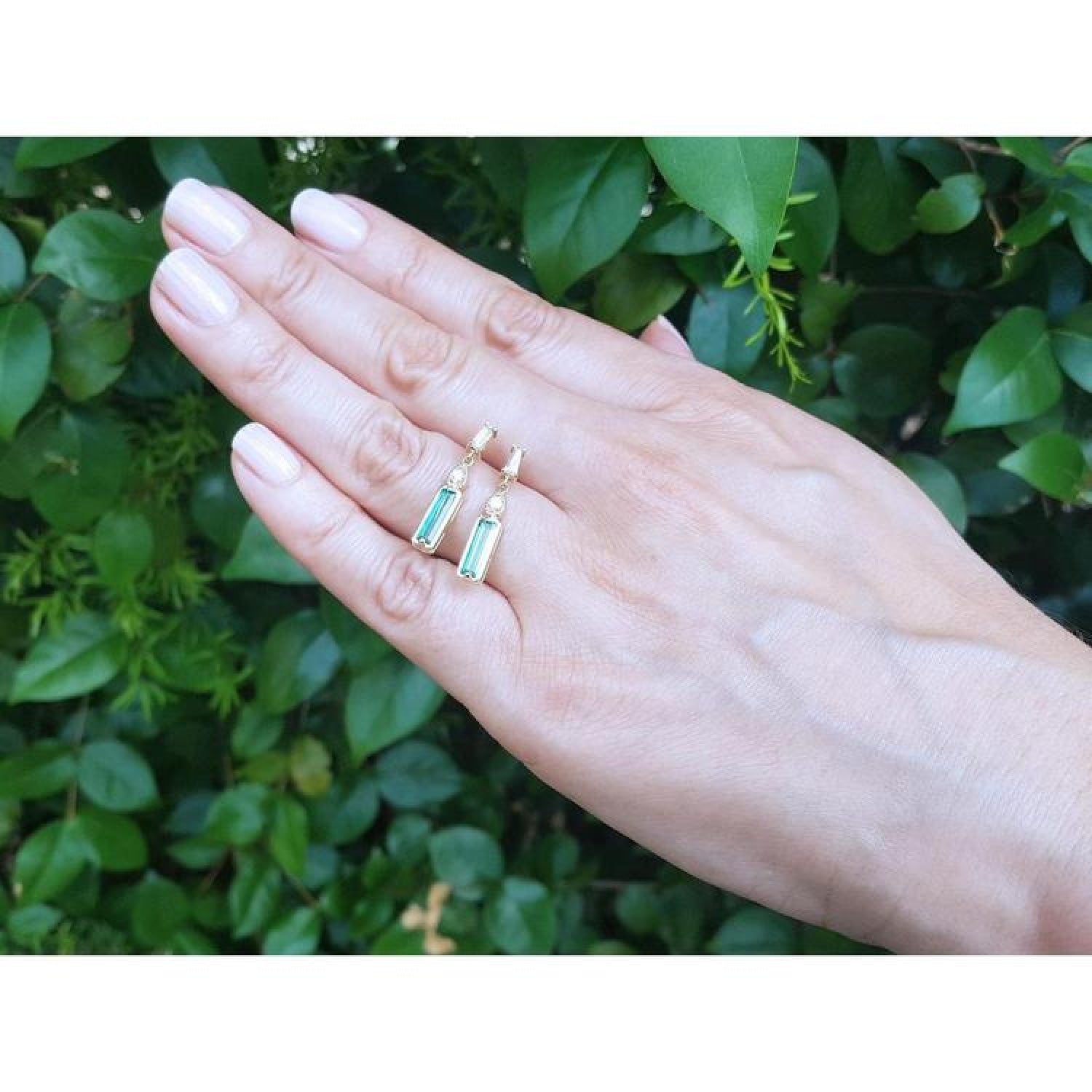 14K gold stud earrings with baguette-cut Colombian emeralds, pear-shaped extensions, and tapered baguette diamonds.