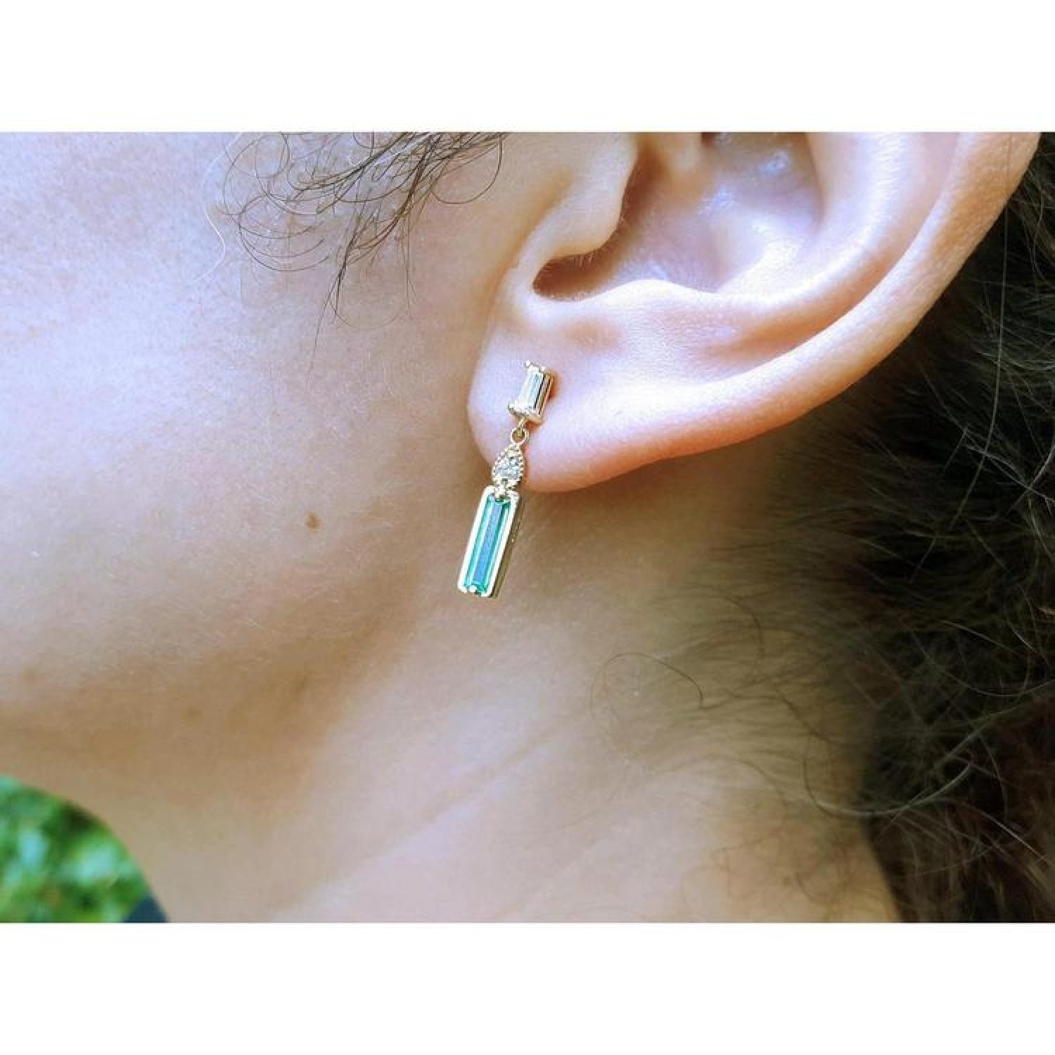 14K gold stud earring with baguette emerald, pear-shaped diamond, and tapered baguette diamonds.