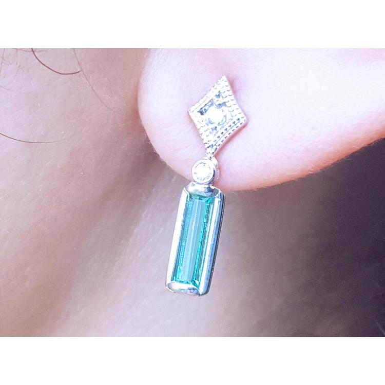 Close-up of a 14k white gold emerald earring with accent diamonds worn on an ear.