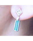 Close-up of a 14k white gold emerald earring with accent diamonds worn on an ear.