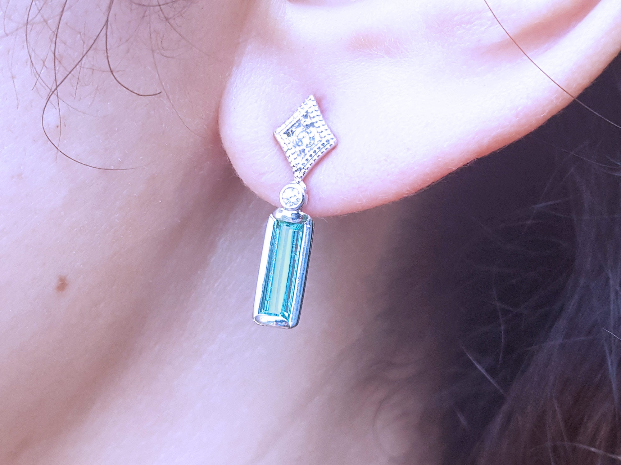 Close-up of a diamond and natural emerald earring on an ear.